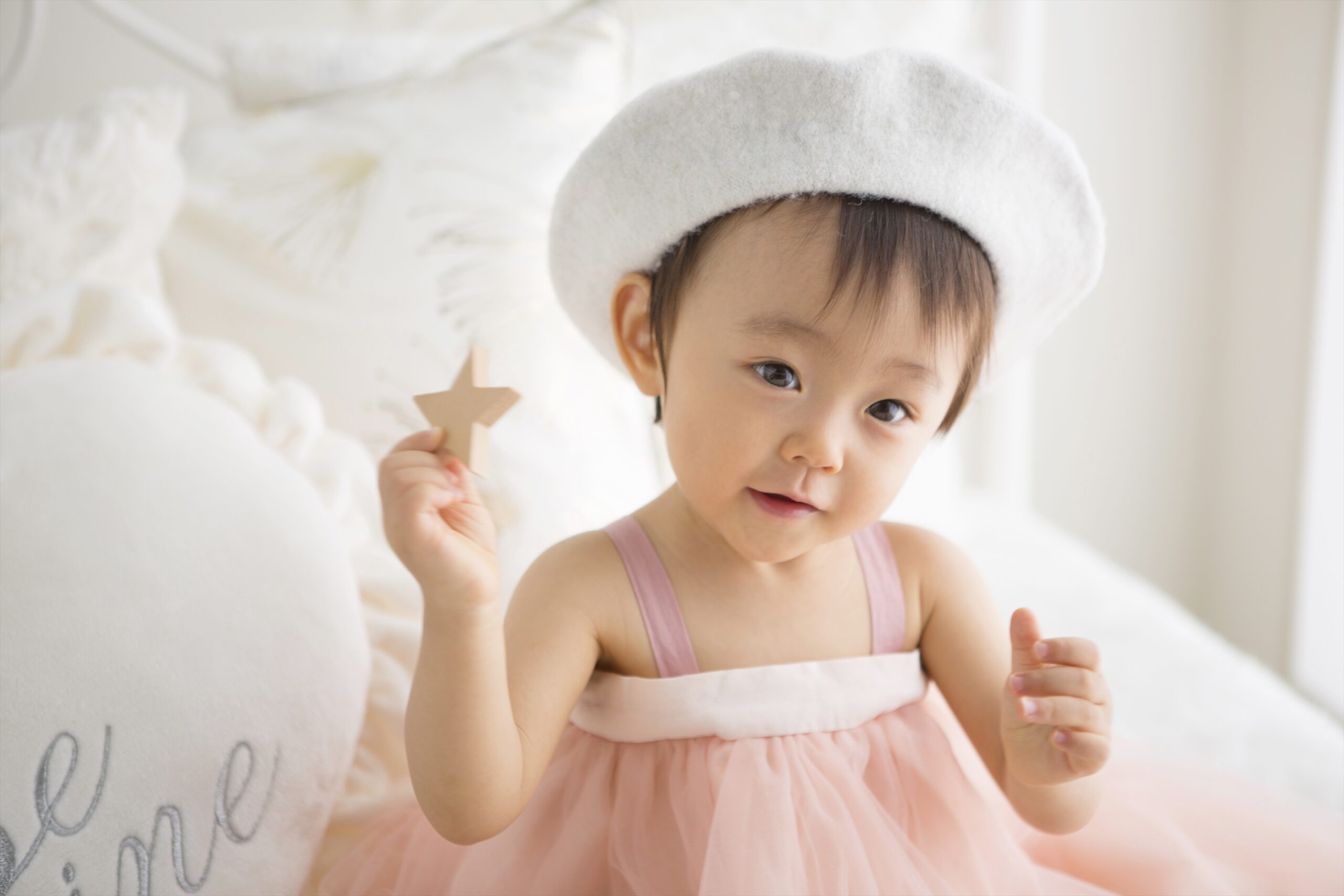 白いベレー帽をかぶりピンクのチュールで星の積み木を掲げる一歳の女の子