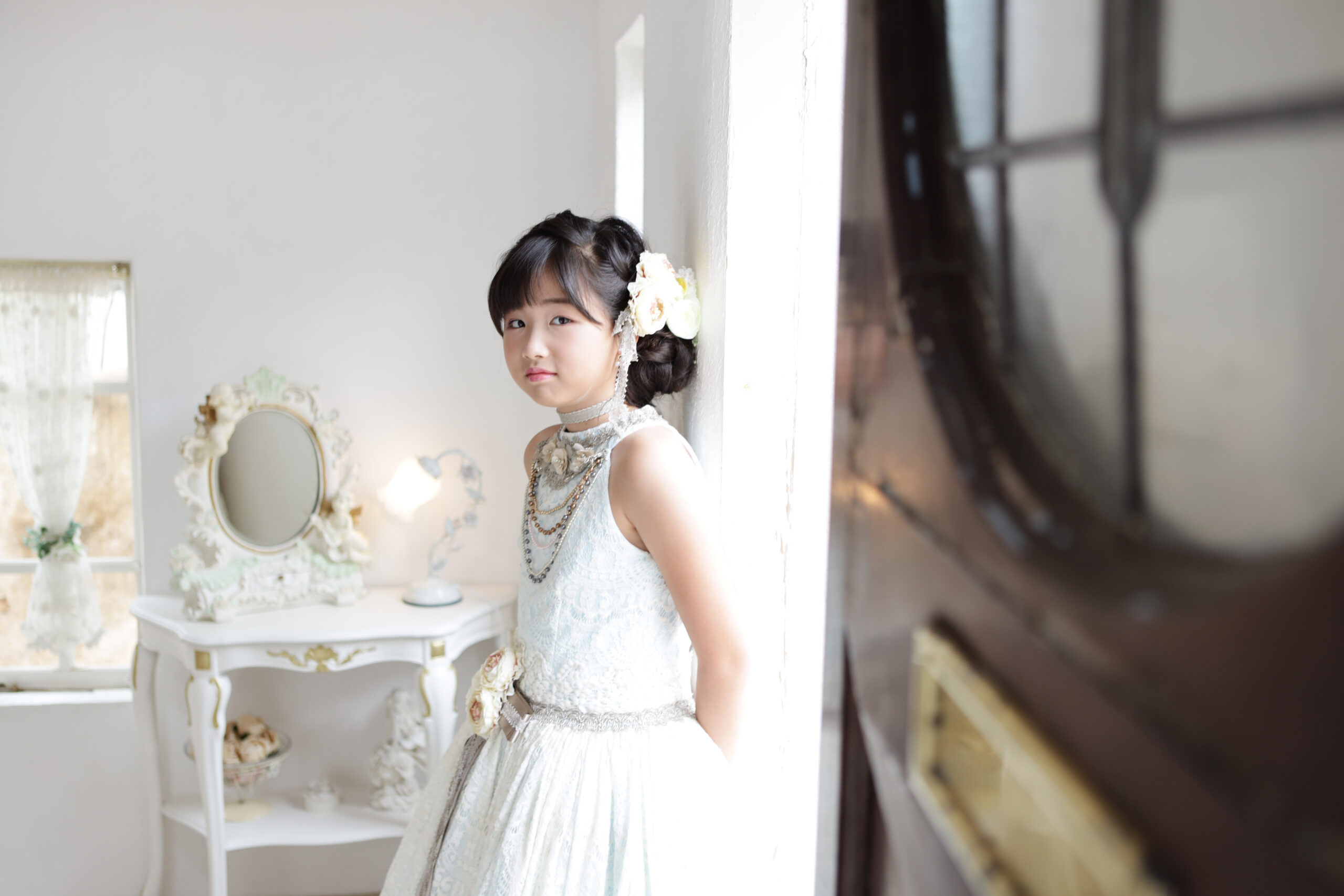 アンティーク調の室内で水色のレースドレスを着て振り返る女の子