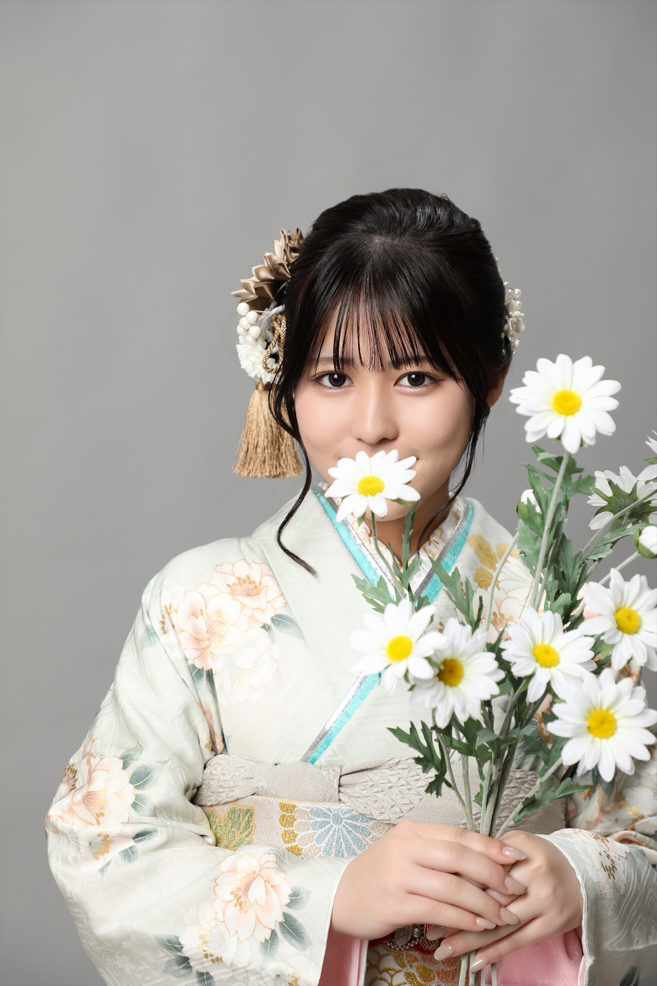 淡い若草色に牡丹をあしらった振袖で白い菊の花束を抱く新成人