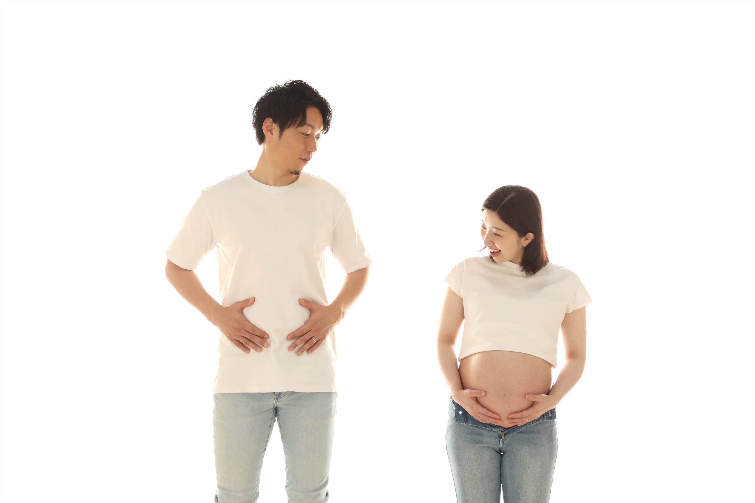 白背景でおなかを抱えるポーズを真似するご夫婦のマタニティ