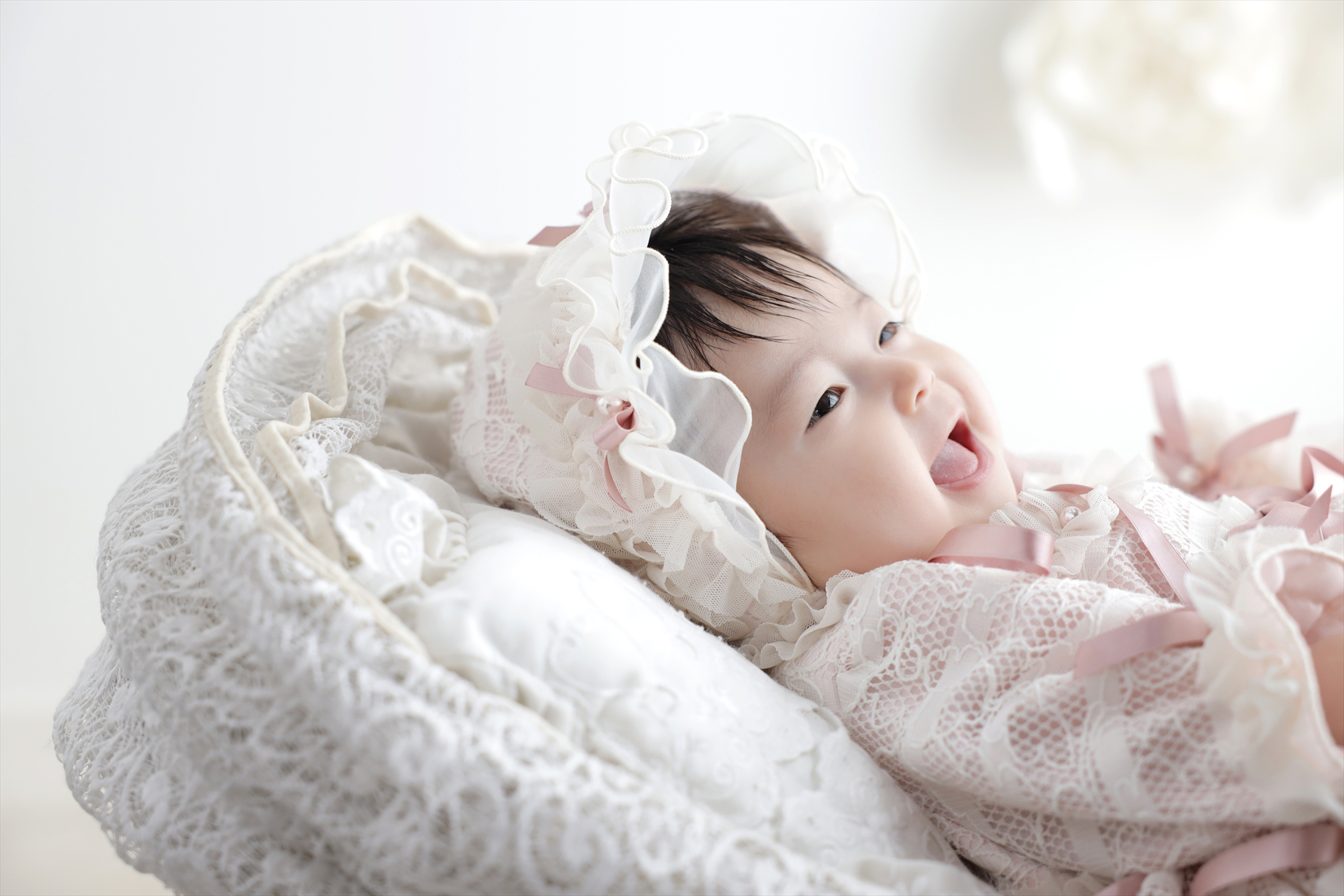白いレースのボンネットをかぶり声をあげて笑う赤ちゃん
