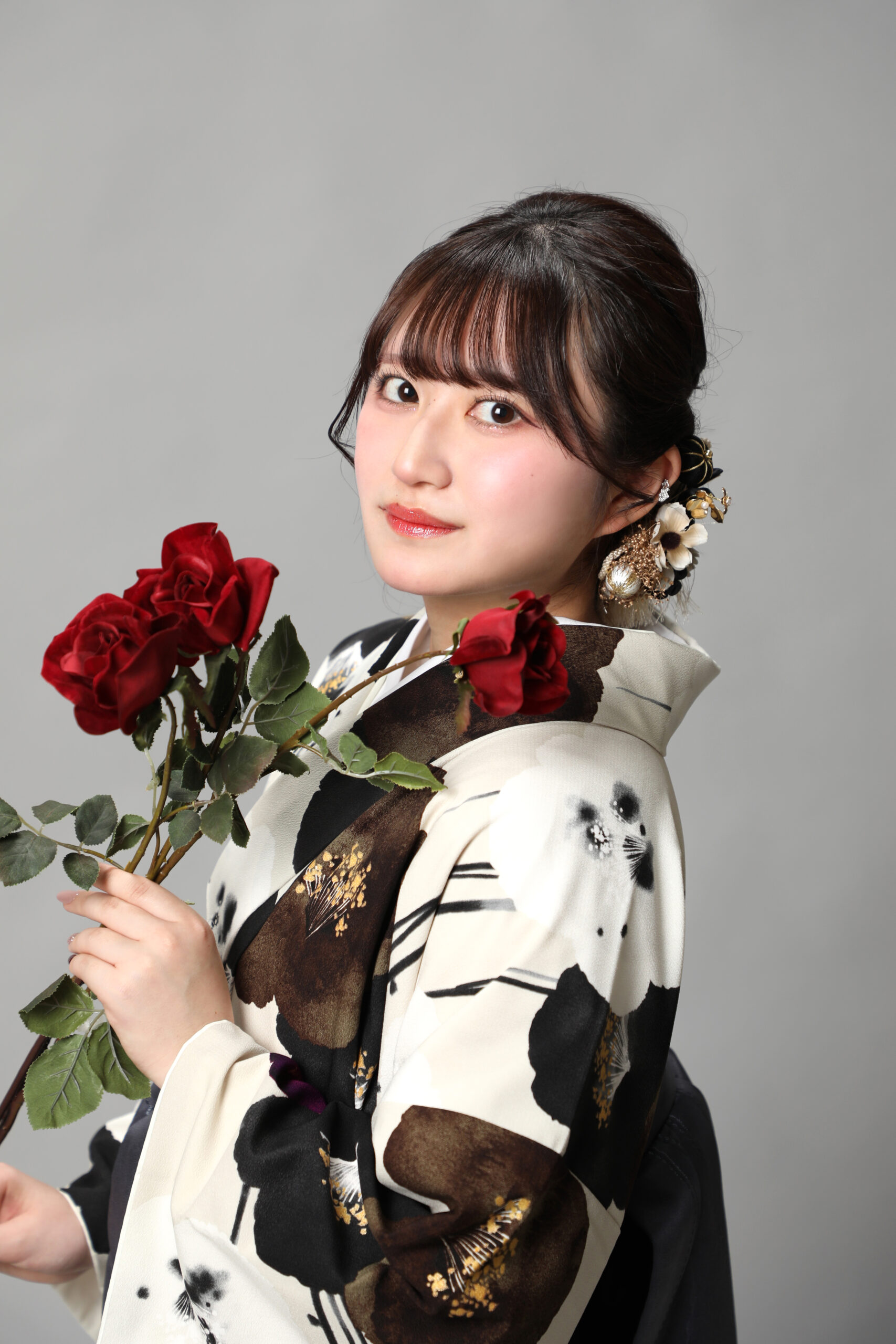 白椿柄の着物をまとい赤い薔薇を胸元へ引き寄せて微笑む横顔