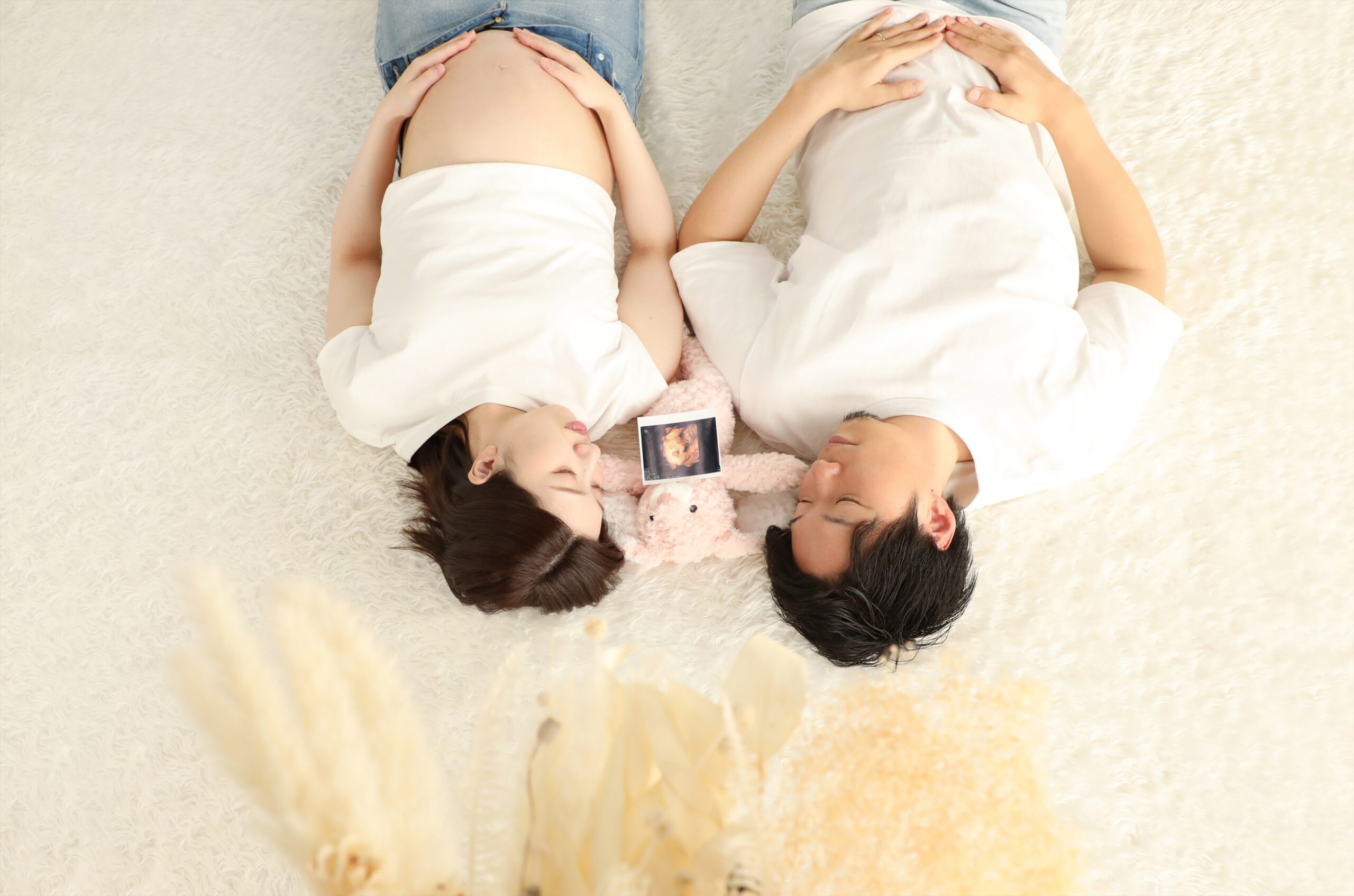 寝転んで並びエコー画と小さなぬいぐるみを間に置いたご夫婦