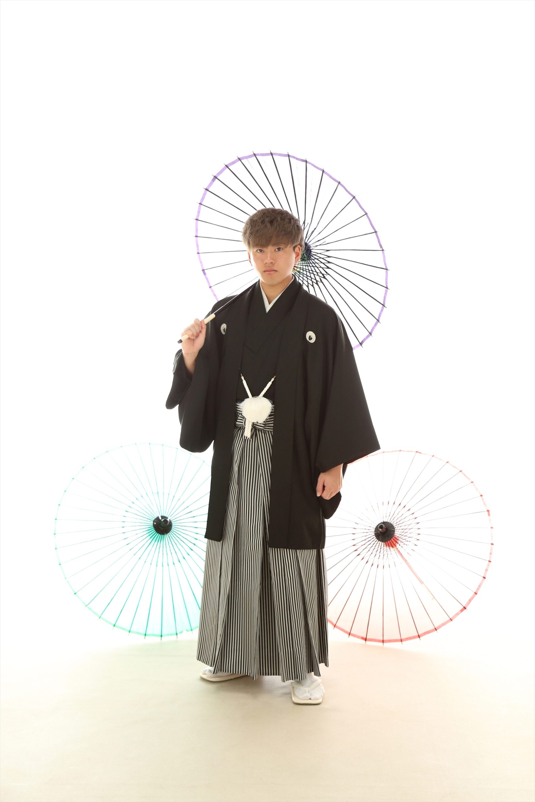 白背景に色とりどりの和傘を配し黒紋付羽織と縞袴で立つ新成人
