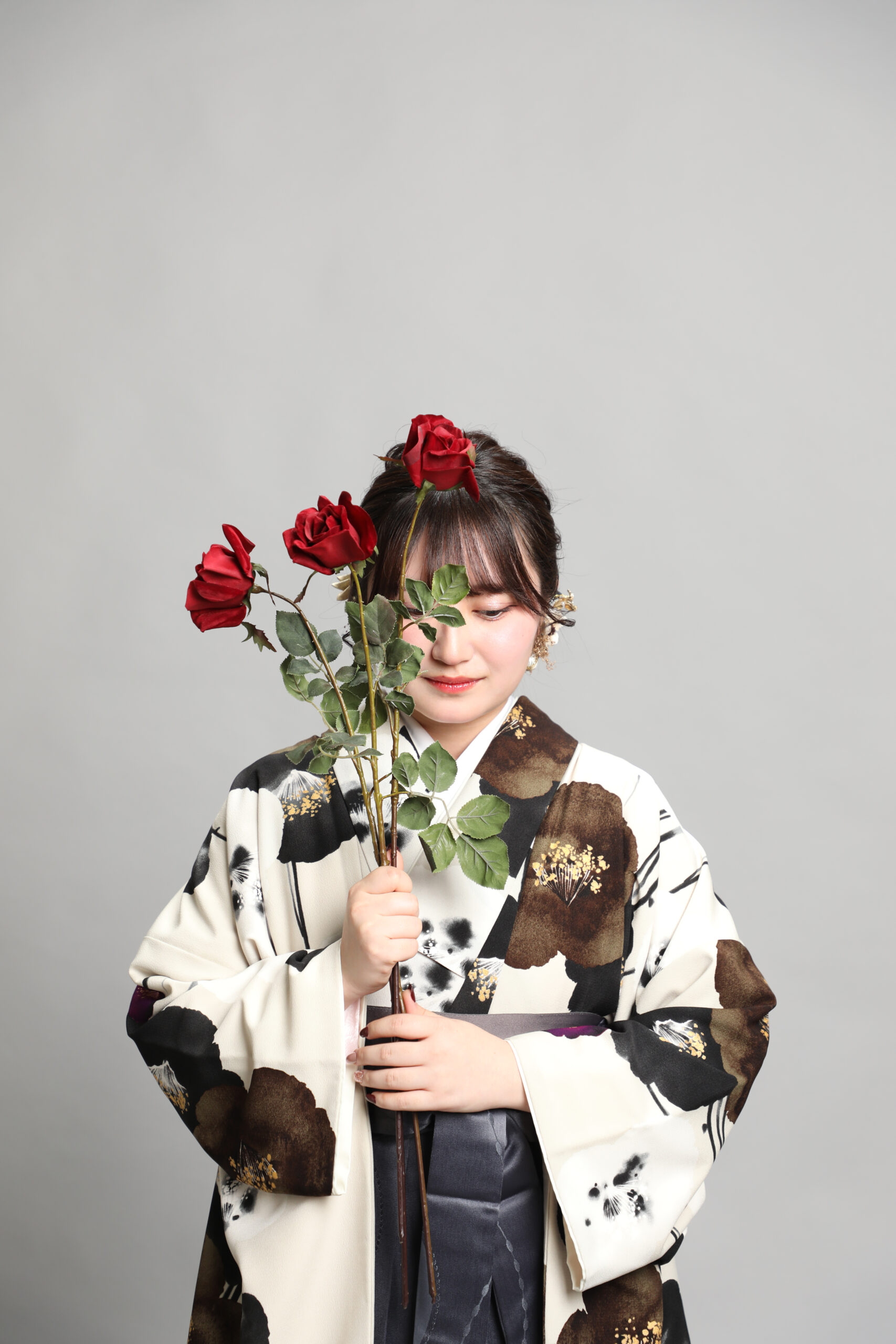 三輪の薔薇を顔の前に立ててそっと目を伏せる椿柄の着物と黒袴