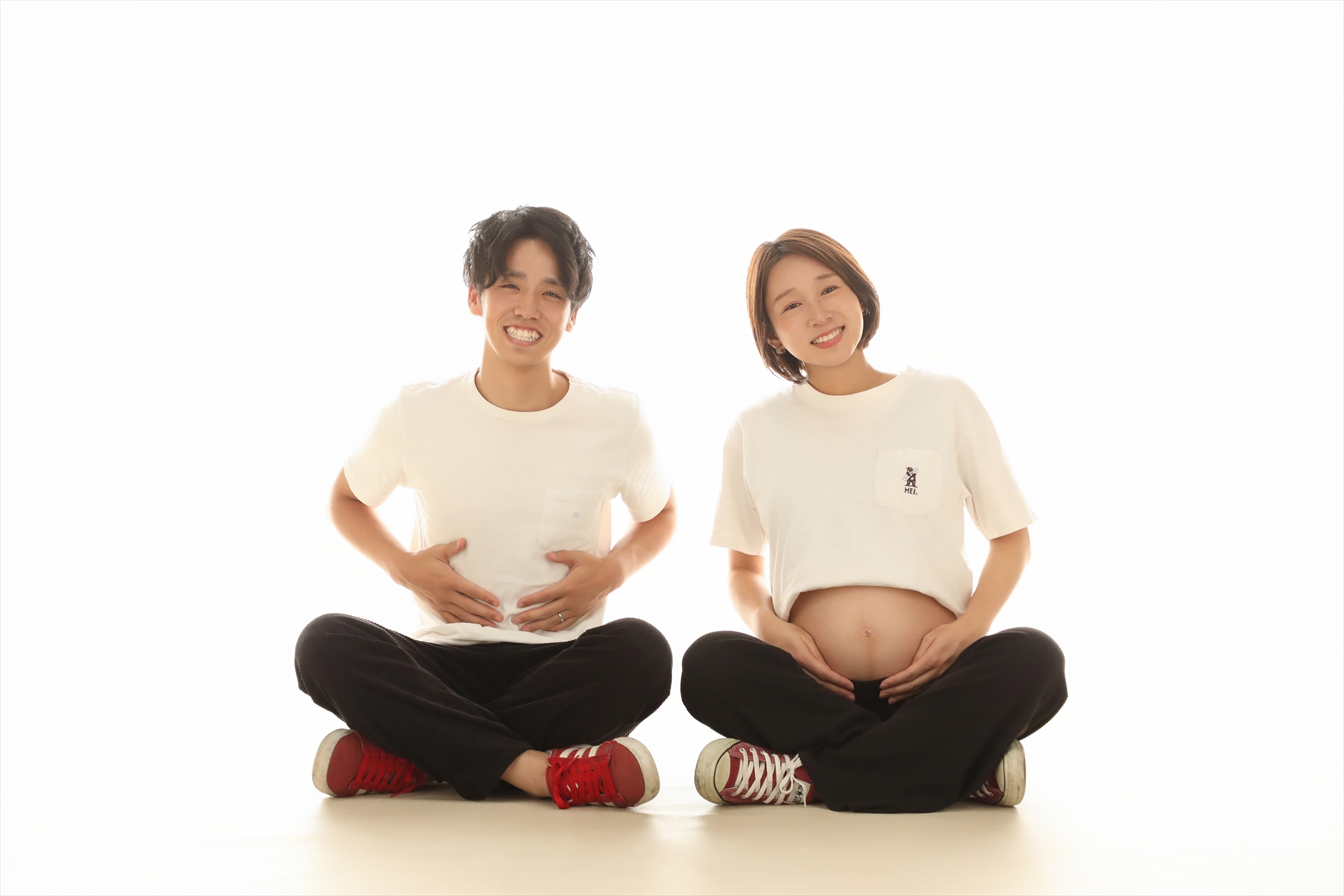 床にあぐらをかいて並びおなかに手を添えるご夫婦の笑顔