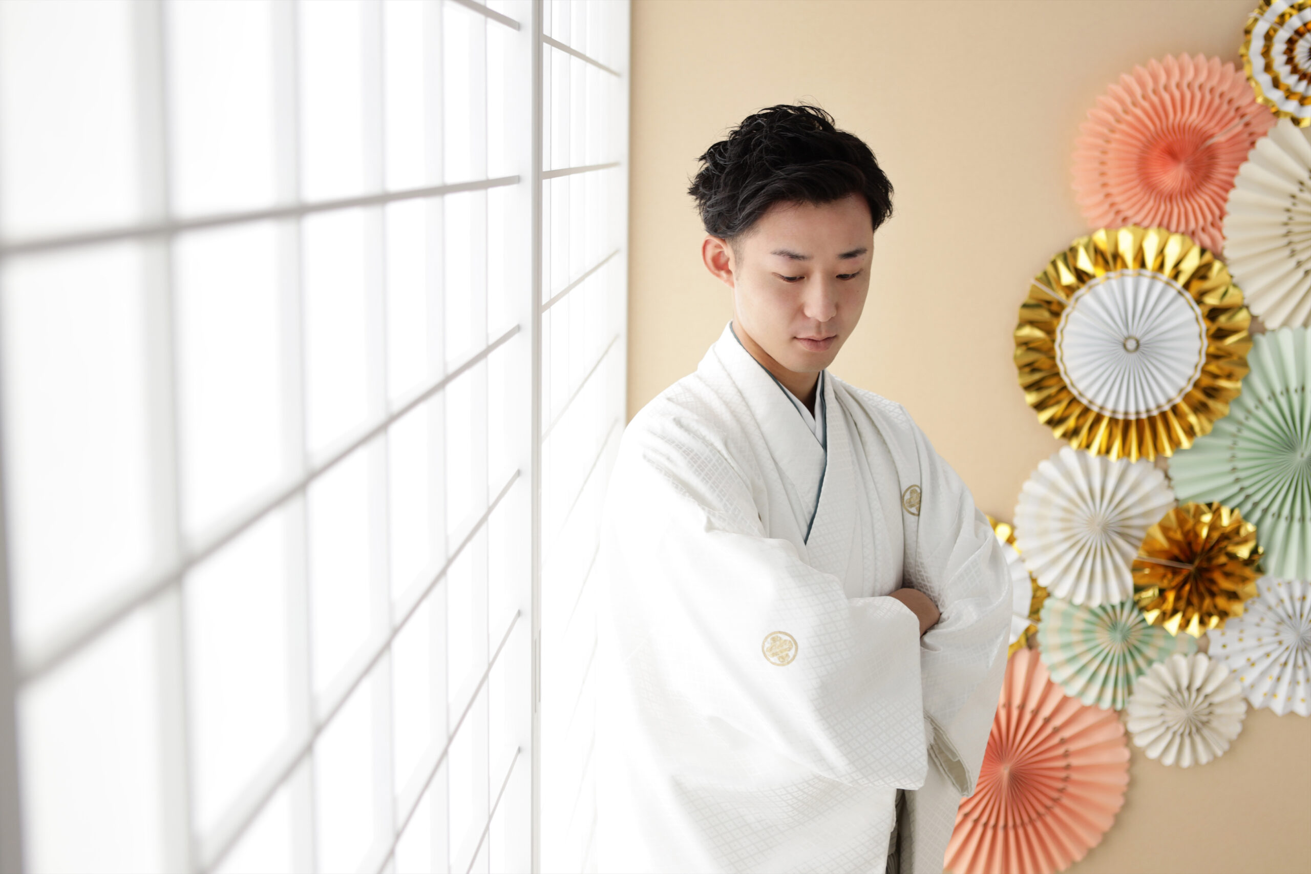 障子の光を受けて腕を組む白い紋付羽織の男性とペーパーファンの壁