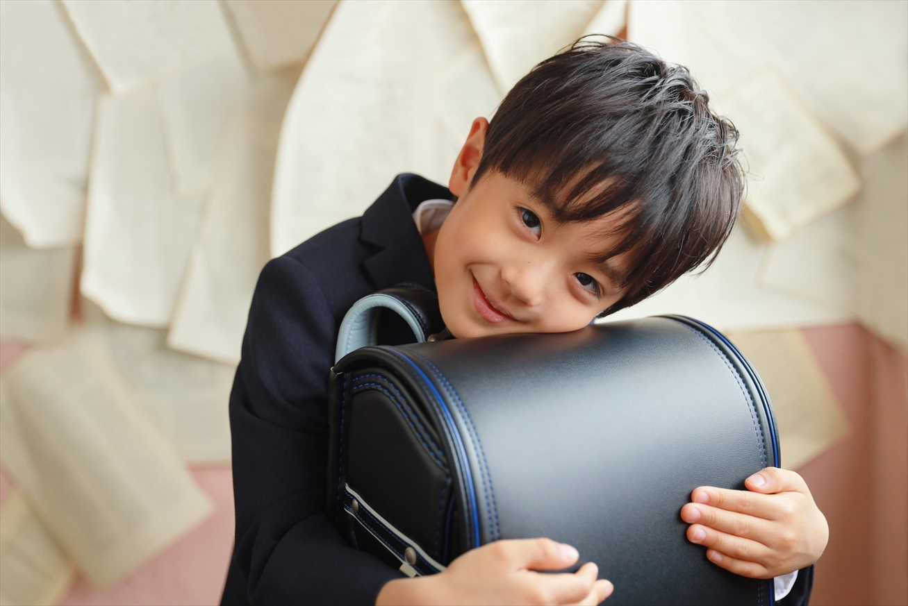 紺のジャケットで青いラインのランドセルを大切そうに抱きしめる男の子
