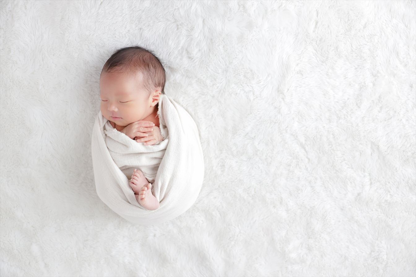 白いファーの上で手足を折りたたみ静かに眠る新生児