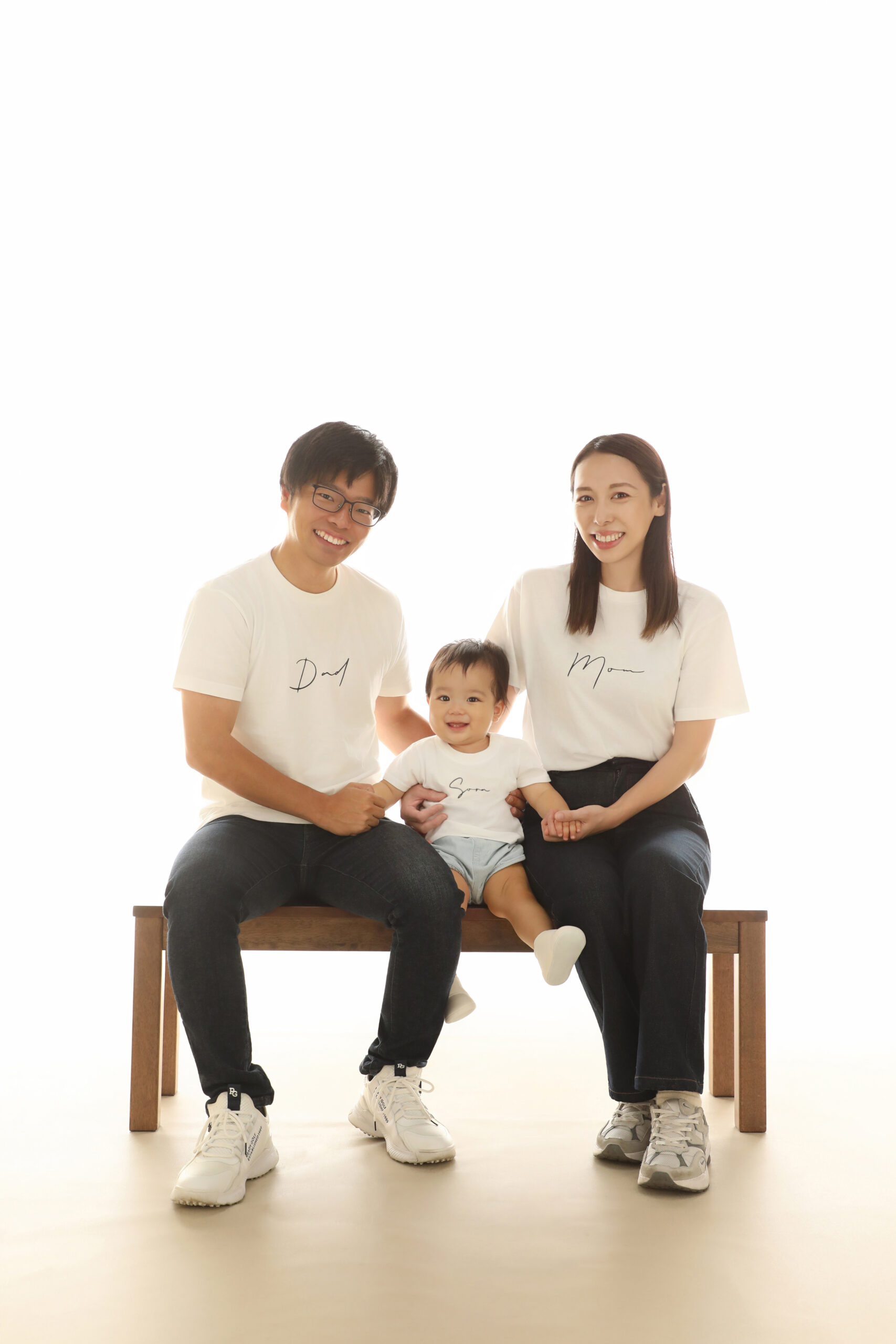 おそろいの白Tシャツでベンチに並ぶご両親と一歳の子どもの記念