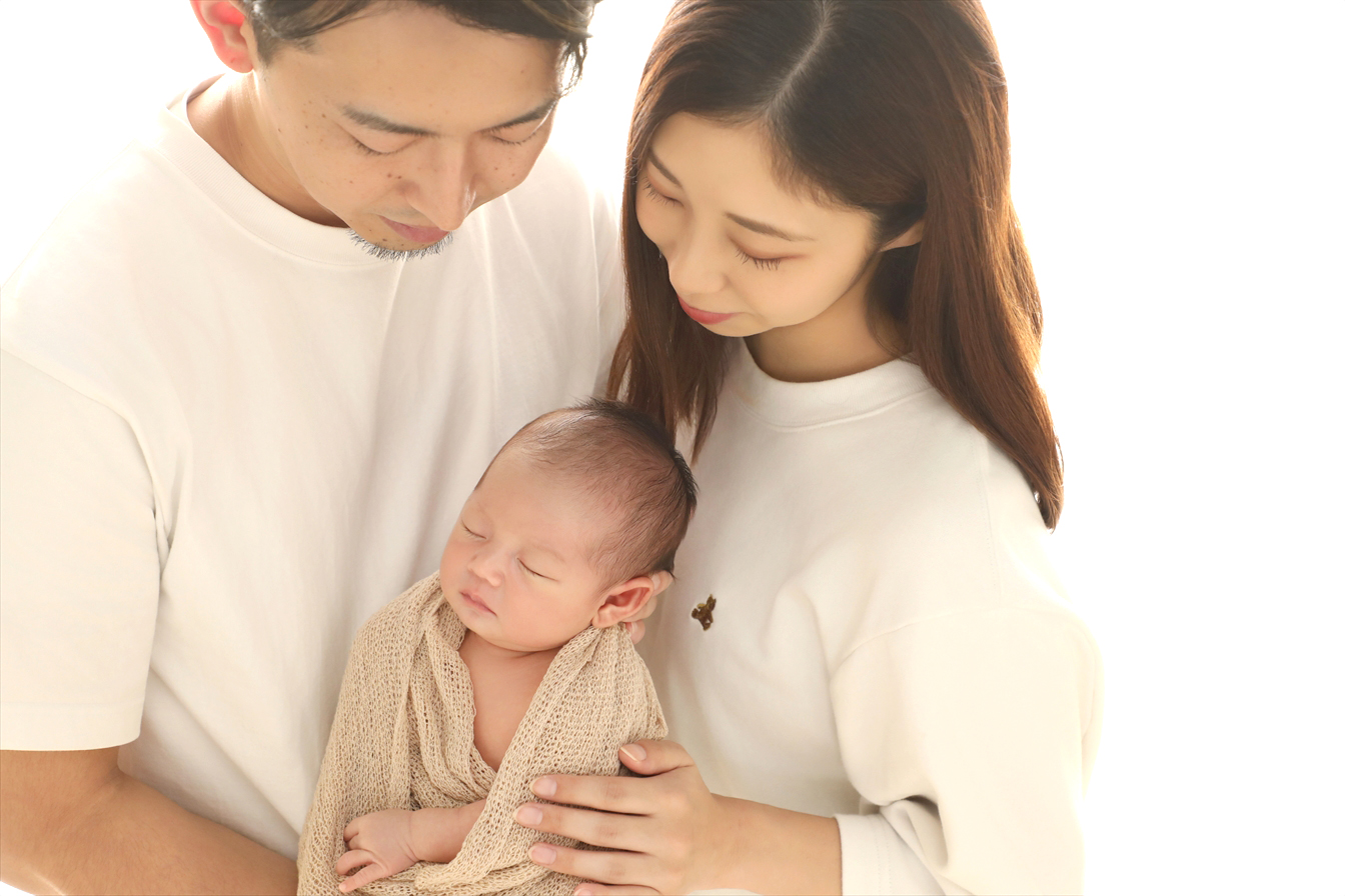 生成りのおくるみに包まれた我が子を見つめるご夫婦