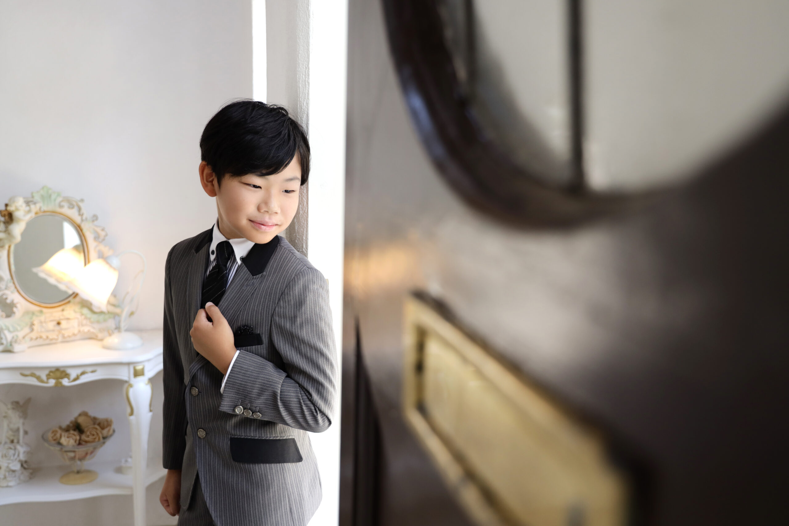 グレーのストライプスーツで襟元に手をかける十歳の男の子
