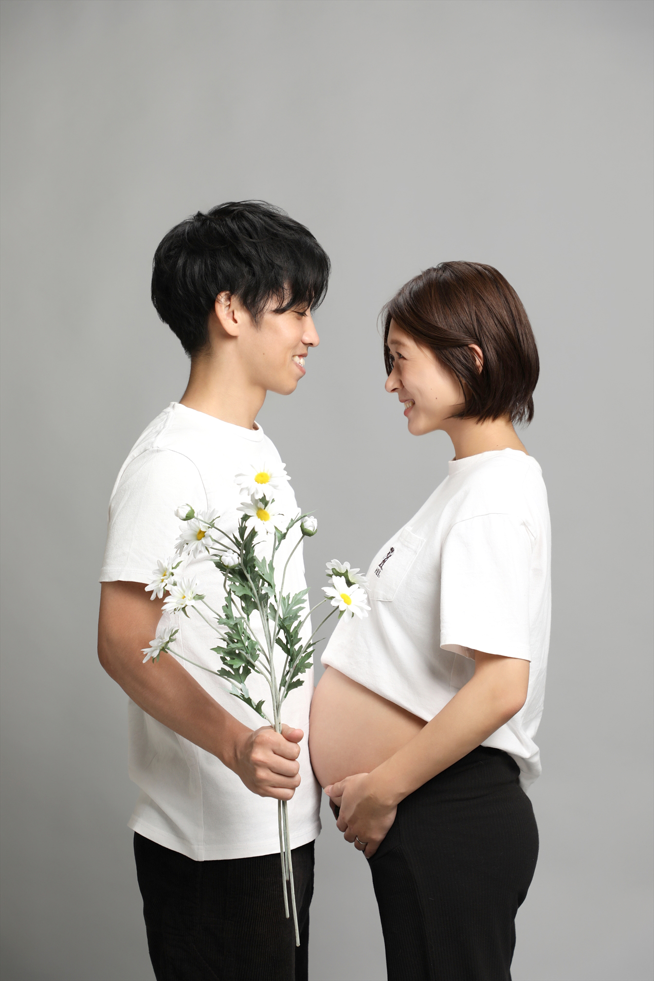 白い花束を手にした夫と見つめ合うマタニティのご夫婦