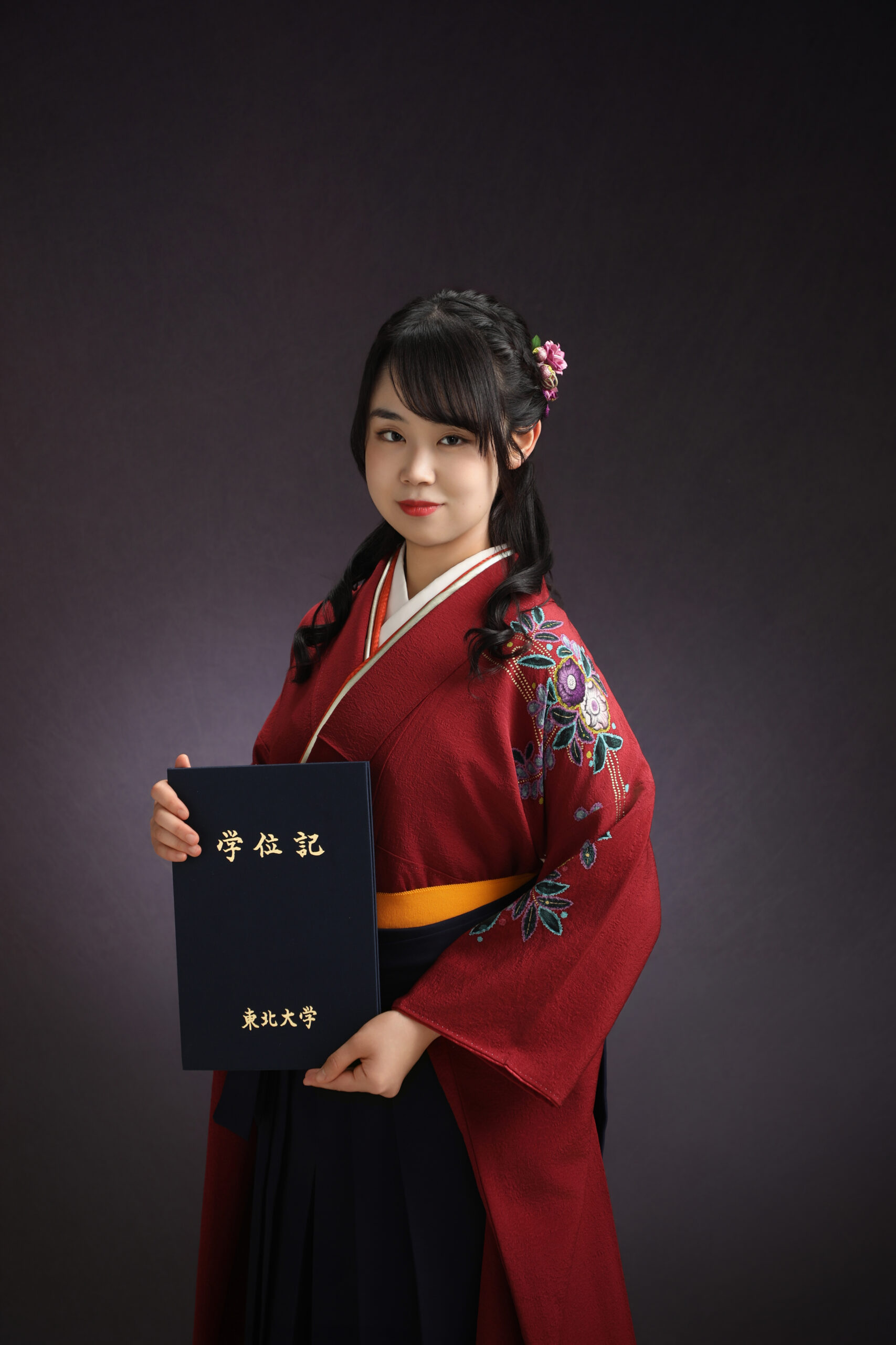 学位記を胸の前に掲げ刺繍入りの臙脂色の着物と紺袴で正面に応える