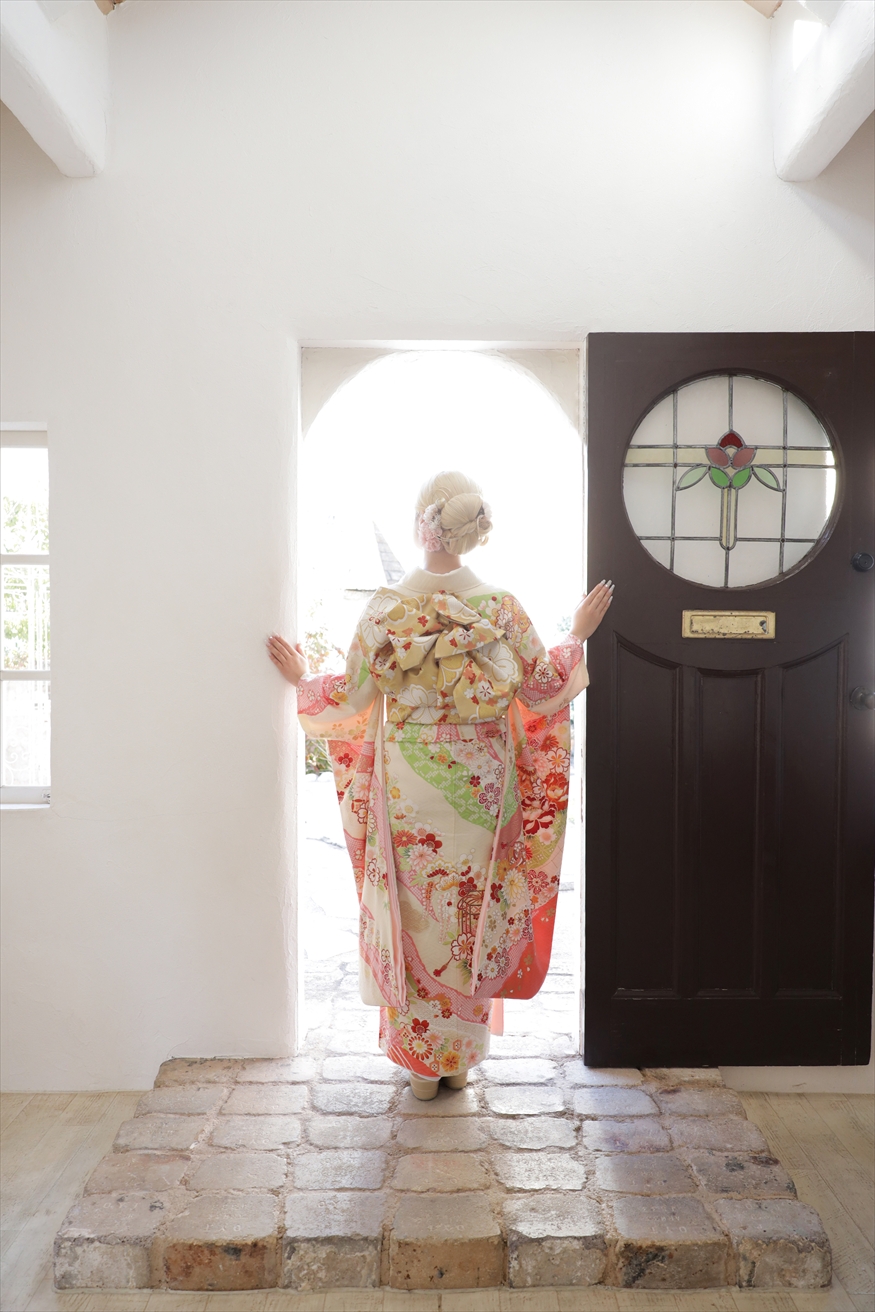洋館の扉を開け背を向けて立つクリーム地に花柄の振袖姿の女性