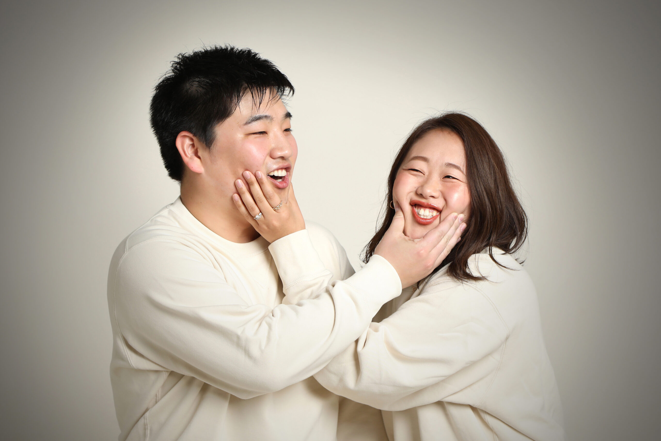 おそろいのスウェットでお互いの頬を押し合っておどけるご夫婦