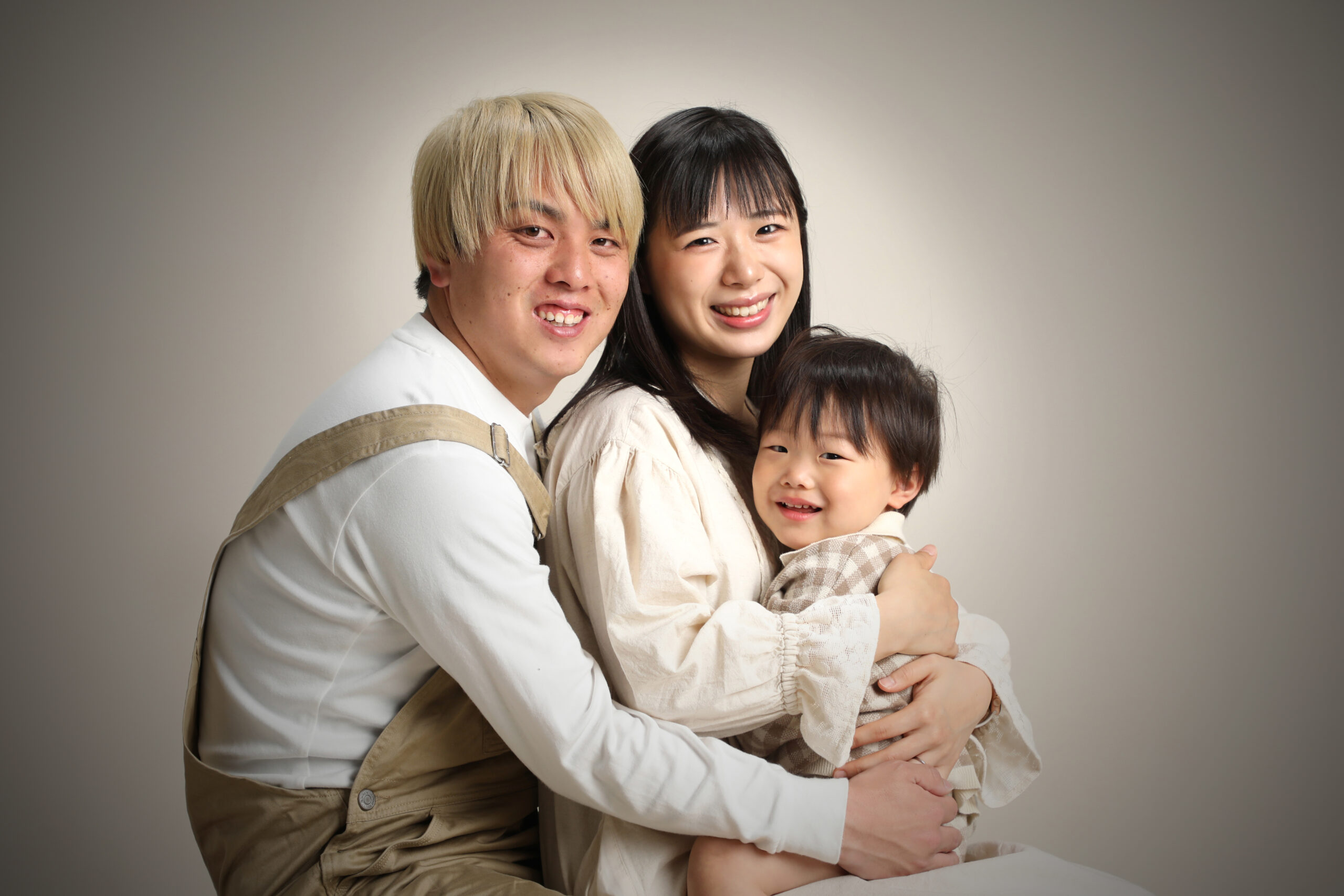 小さな男の子を真ん中に抱き寄せて笑う若いご両親