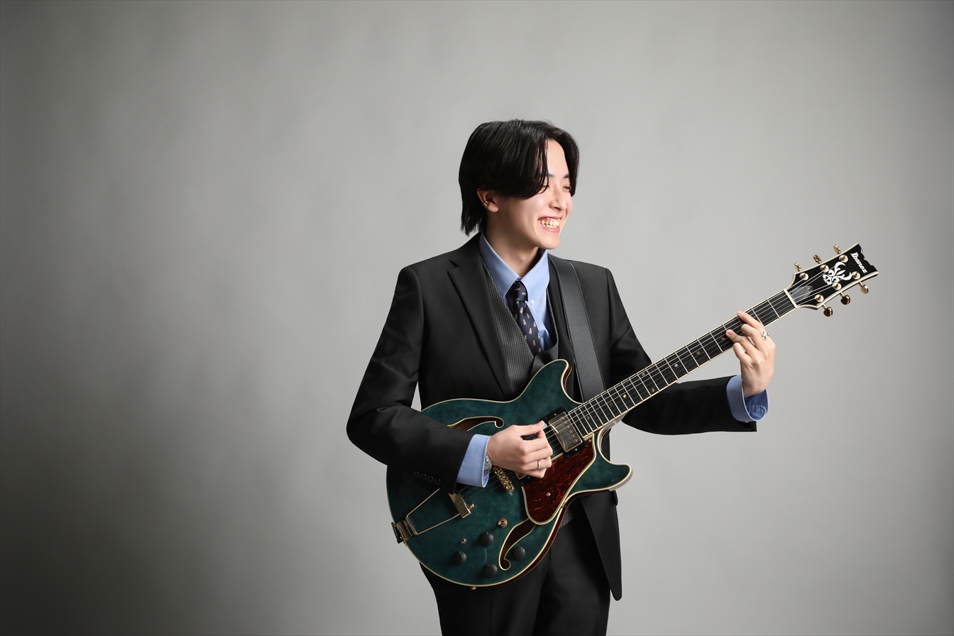 スーツ姿でギターを抱え声をあげて笑う男性のスタジオポートレート