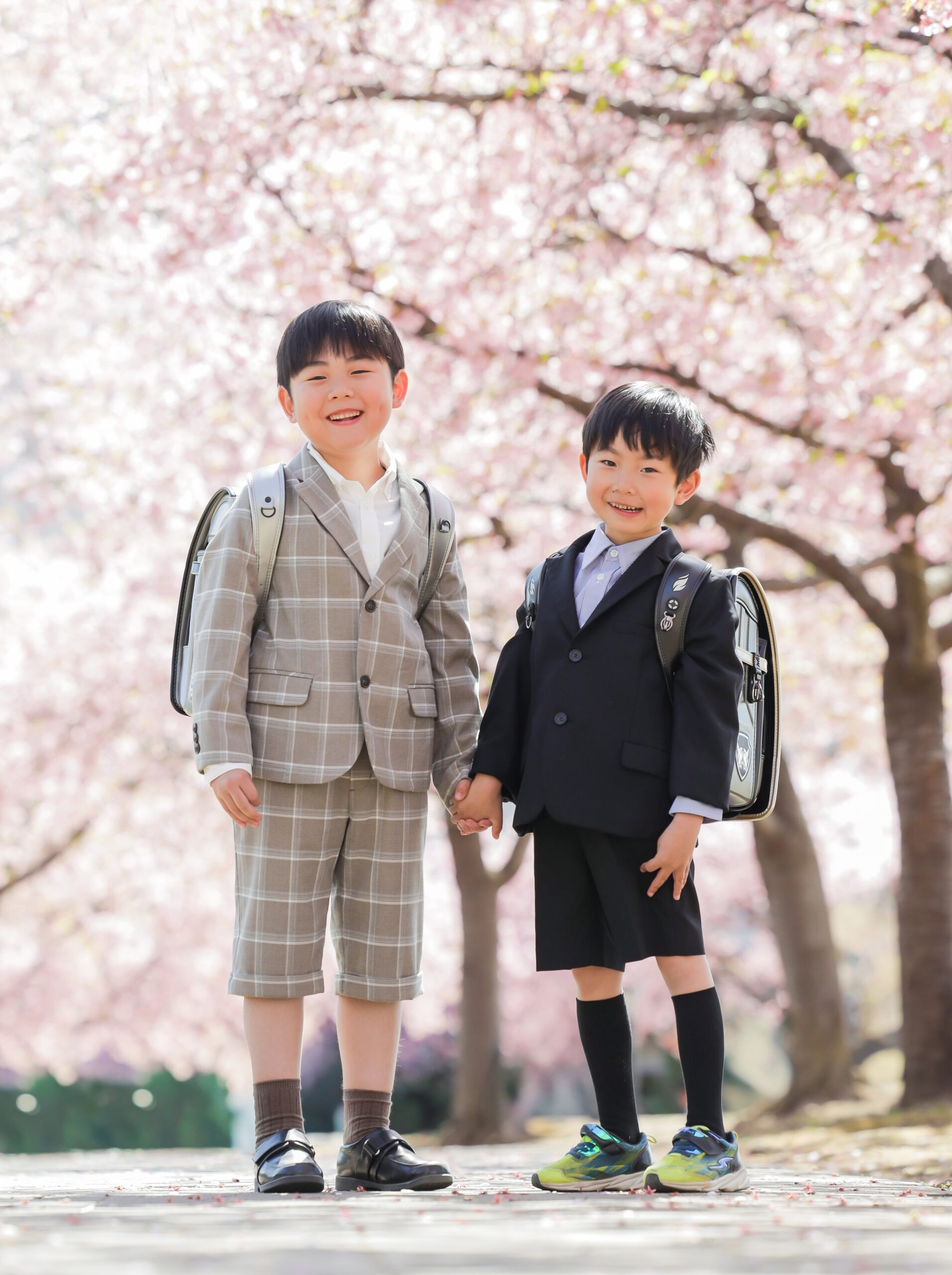 城址公園の河津桜の下でランドセルを背負い手をつなぐ新一年生の男の子ふたり